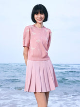 A lady wears a knit top and a pink skirt.